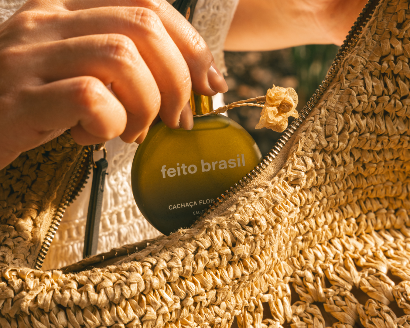 Perfume feminino para brinde corporativo de luxo da marca feito brasil, Cachaça Flor de Jambu, com foto mostrando modelo colocando o perfume miniatura em bolsa de palha brasileira.